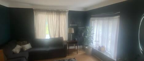 Ett vardagsrum med en soffa i mörk färg, en mönstrad matta, ett litet bord med en lampa och en krukväxt.