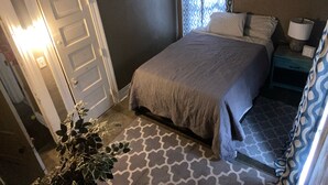 A bedroom with a bed, a nightstand, a lamp, a potted plant, and a door. - Spacious 4-bedroom Historic house with WiFi in heart of Detroit/Free Parking! (Detroit)