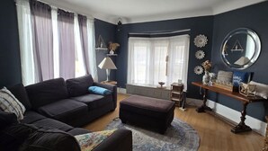 A living room with a dark blue wall, a black sofa, a round coffee table, and a wooden floor. - Spacious 4-bedroom Historic house with WiFi in heart of Detroit/Free Parking! (Detroit)