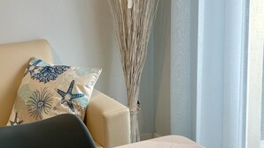 Une chambre d’hôtel bien rangée, avec un lit, une table de chevet sur laquelle se trouvent une tasse, un mug et une cuillère, un vase décoratif contenant des plantes séchées et un coussin à motifs.