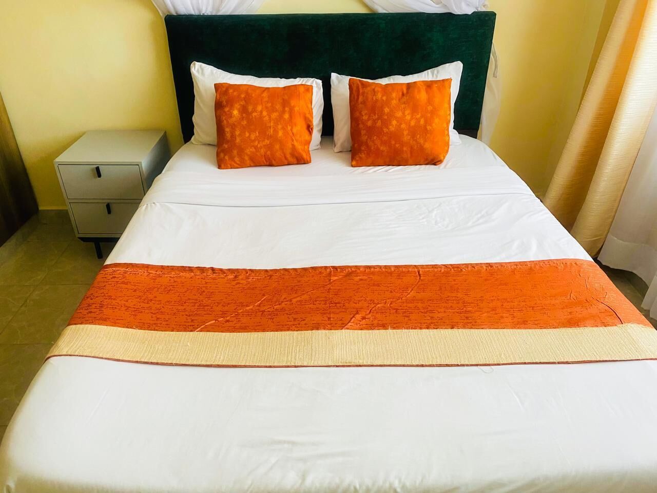 A bed with white and orange bedding, a green headboard, and a small bedside table.