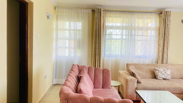 Un salon avec un canapé rose, un canapé beige et une petite table.