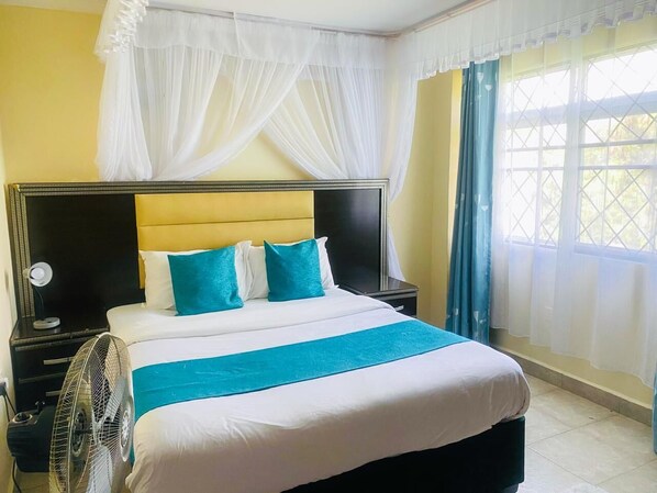 Una habitación de hotel con cama, mesita de noche, ventilador y ventana con cortinas.