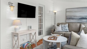 Una sala de estar moderna con un televisor de pantalla plana, muebles blancos y un cuadro en la pared.