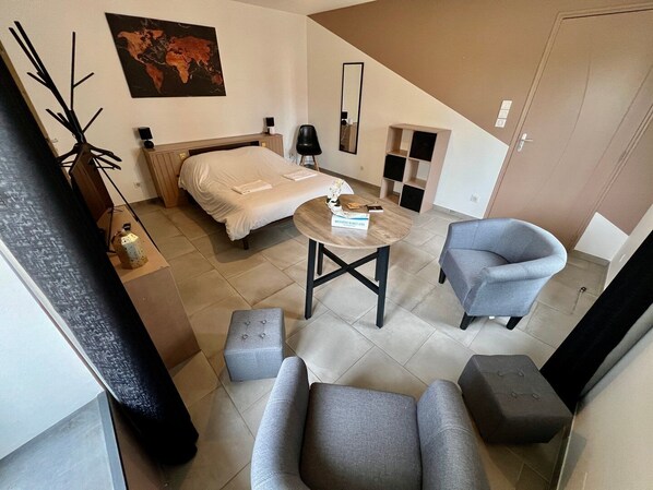 Une chambre d’hôtel moderne comprenant un lit, une table ronde, deux fauteuils, une petite table d’appoint, une carte du monde accrochée au mur et une porte.
