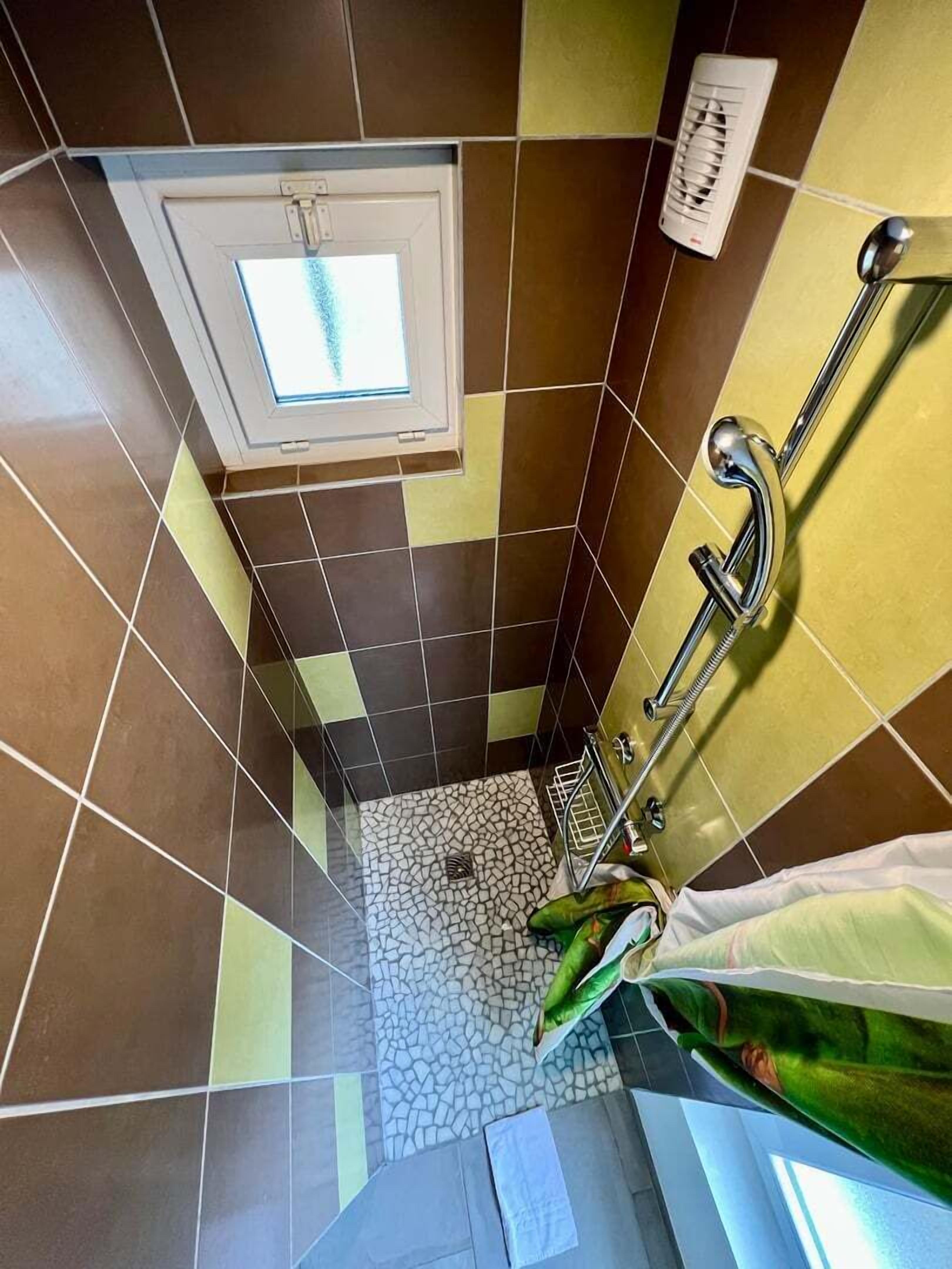 A bathroom with a tiled floor, a shower area, and a window.