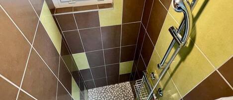 A bathroom with a tiled floor, a shower area, and a window.