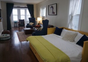 Una habitación de hotel con cama, sillón, sofá, lámpara y ventana.