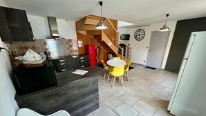 Una cocina moderna con una isla central, un área de comedor con sillas amarillas, una escalera y un reloj en la pared.
