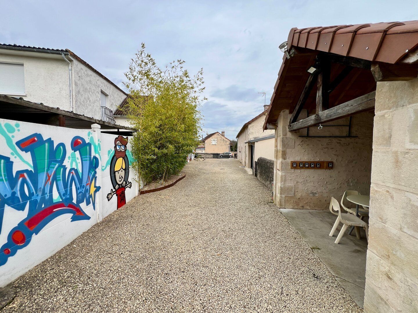 Een smal grindpad dat leidt naar een gebouw met een pannendak en een muur met graffiti.