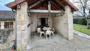 A stone-built outdoor kitchen with a brick oven, a table, and two chairs.