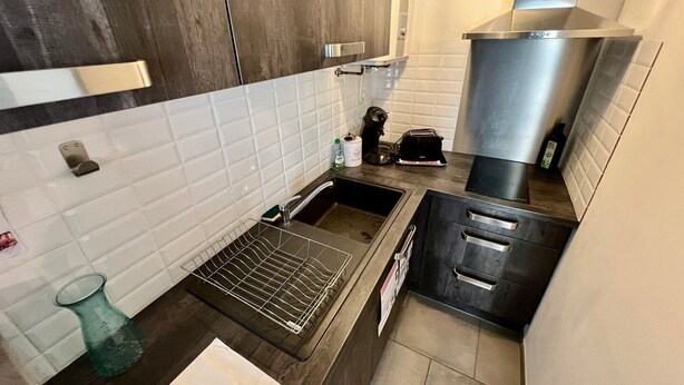 A compact kitchen with white tiled backsplash, dark wooden cabinets, stainless steel appliances, and a black countertop.