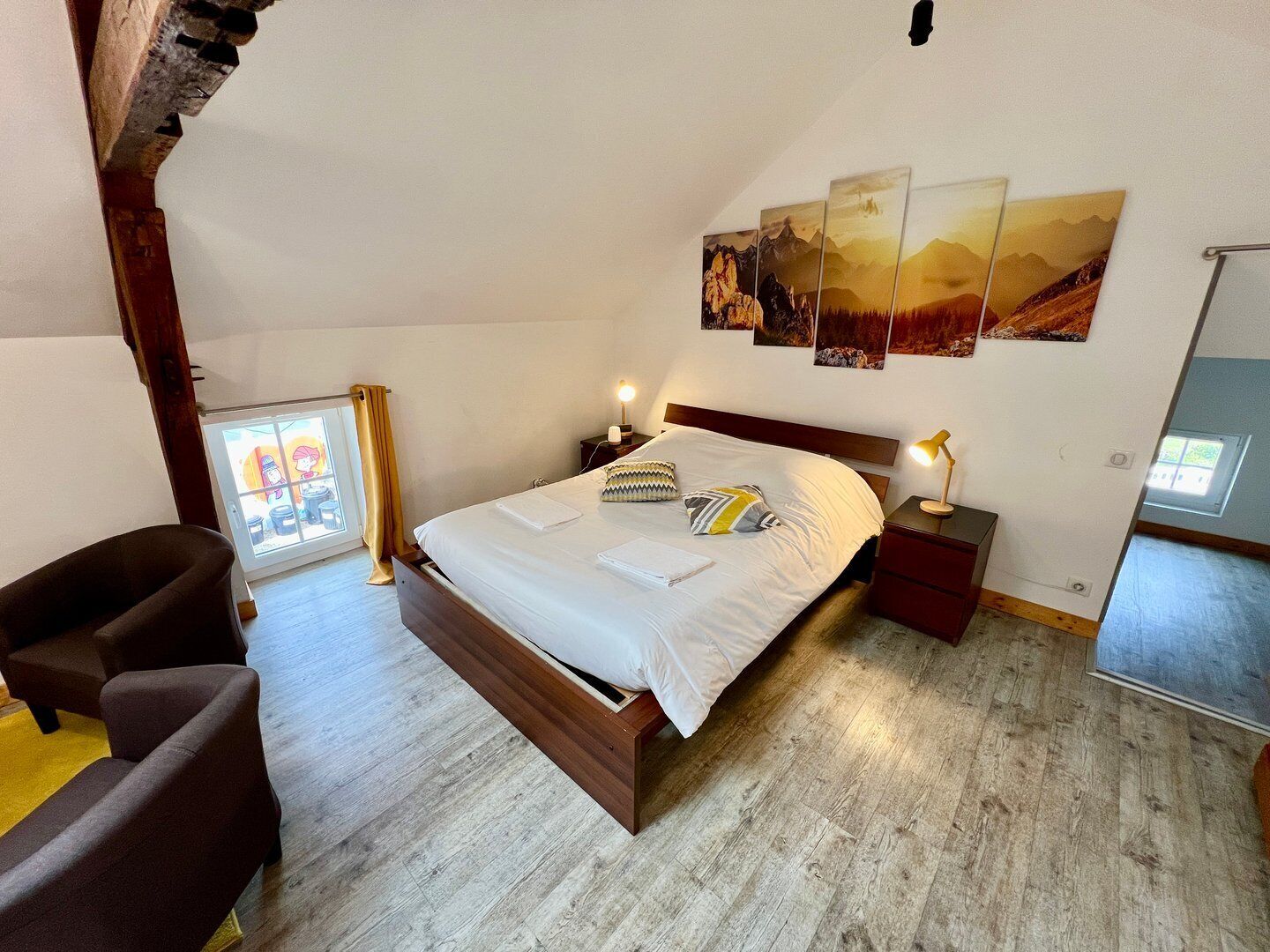 Une chambre à coucher avec un lit, une table de chevet, une lampe, une chaise et une fenêtre avec des rideaux.