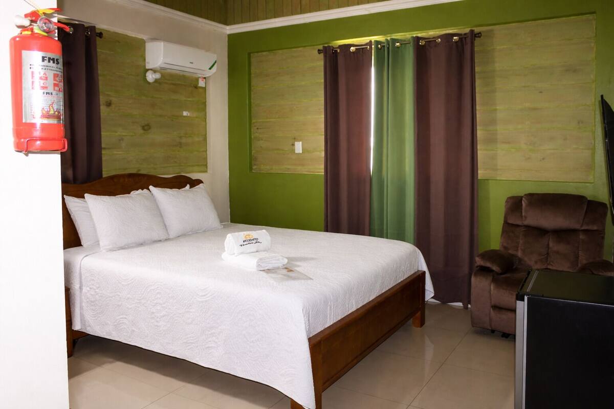 Une chambre d’hôtel équipée d’un lit, d’une chaise, d’un extincteur et d’un appareil de climatisation.