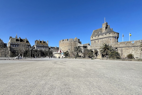 A historic stone castle with a large courtyard, a small pavilion, and flags on the building.
