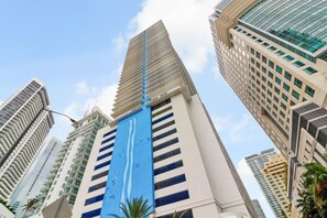 Un immeuble de grande hauteur, caractérisé par une large bande verticale bleue, entouré d’autres bâtiments imposants.