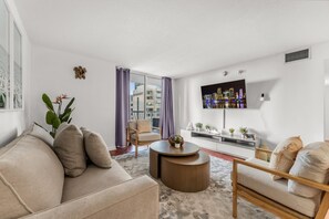 Un salon moderne avec un canapé, des fauteuils, une table basse et un téléviseur fixé au mur.
