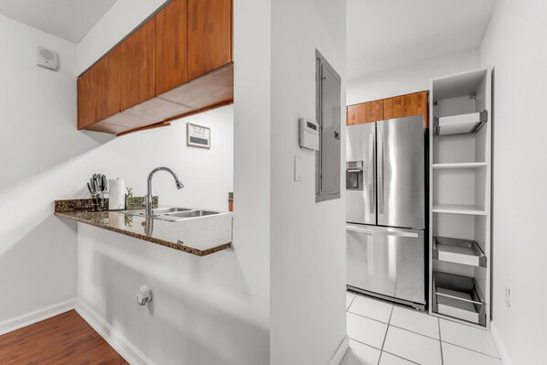 A kitchen with a stainless steel refrigerator, wooden cabinets, a granite countertop, and a built-in sink.