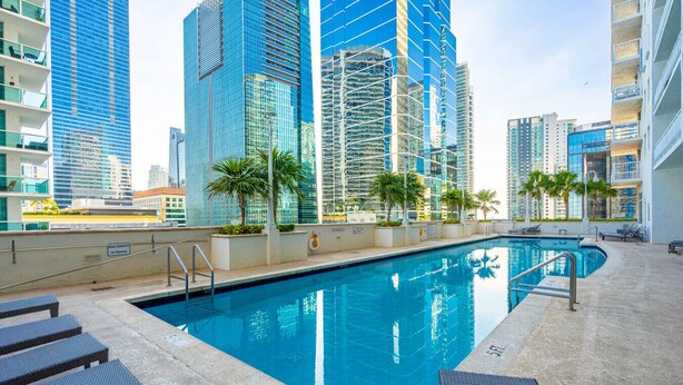 A swimming pool with lounge chairs and palm trees, surrounded by high-rise buildings. - Perfectly Located Miami 3BR with Stunning Views (Miami)