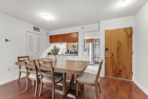 A modern kitchen with wooden cabinets, a stainless steel refrigerator, and a dining area with a wooden table and chairs. - Perfectly Located Miami 3BR with Stunning Views (Miami)