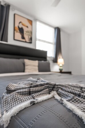 Un lit bien fait, recouvert d’une couverture à carreaux gris et blancs et agrémenté d’un oreiller gris.