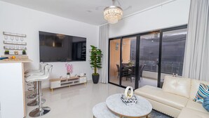 Una sala de estar moderna con sofá, mesa de centro, televisor, comedor y balcón.