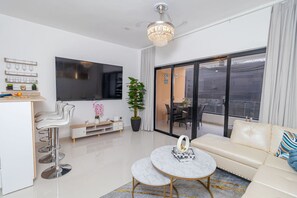 Ein modernes Wohnzimmer mit einer Couch, einem Couchtisch, einem Fernseher, einer Essecke und einem Balkon.