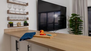 Una cuina moderna amb taulell de fusta, un televisor penjat a la paret i una planta a la dreta.