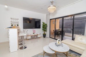 A modern living room with a sofa, a coffee table, a TV, and a balcony with a view.