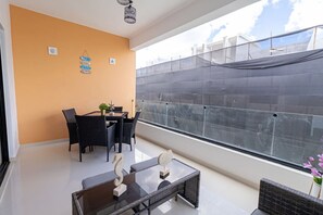A balcony with a glass table, chairs, and a view of the cityscape.
