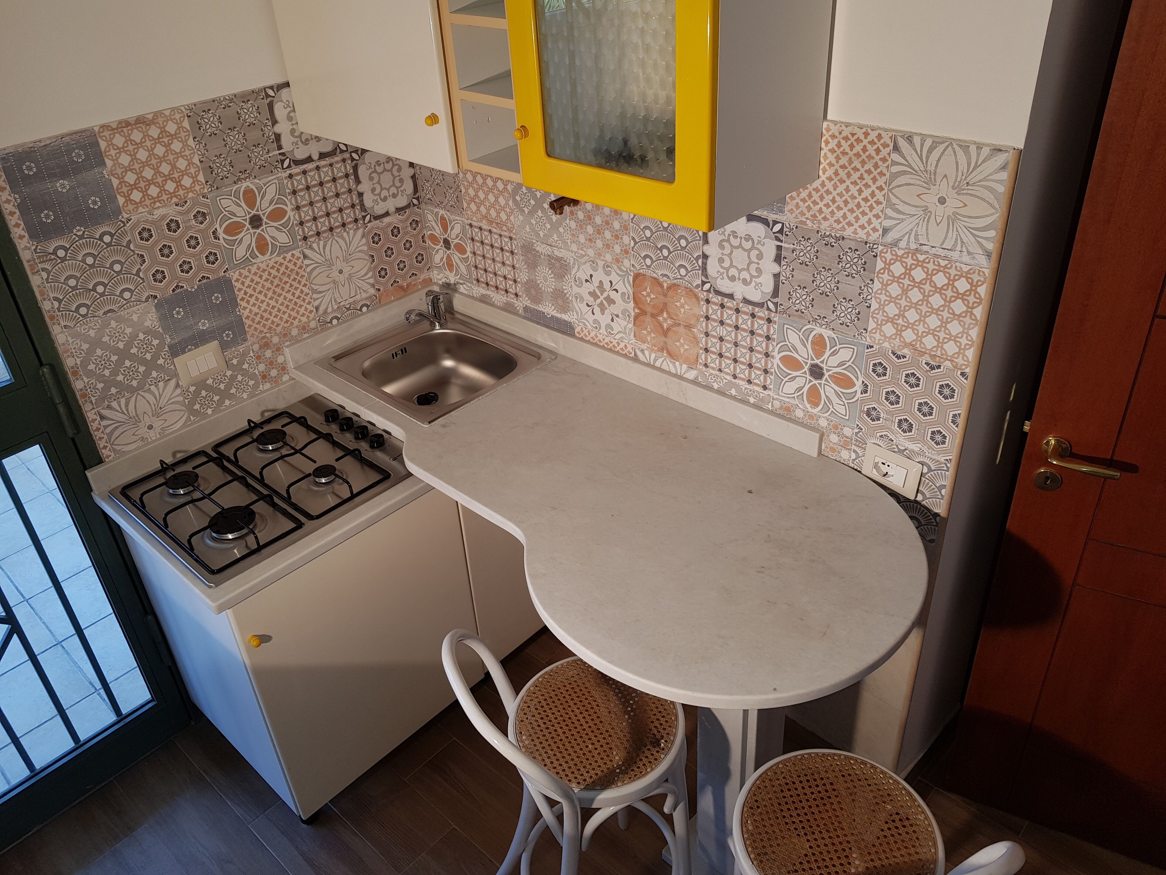 A compact kitchen with a gas stove, a sink, and a small dining area with two wicker chairs.