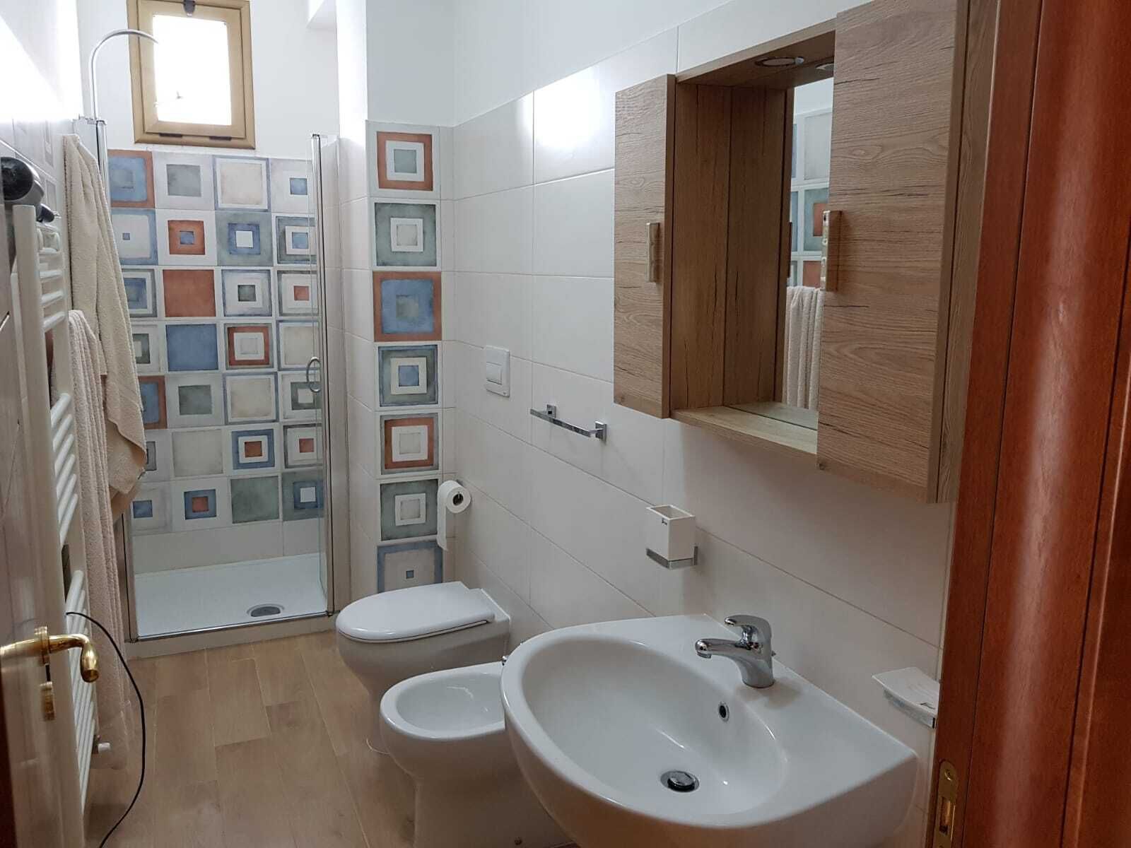 Un baño con ducha, dos inodoros, un lavamanos y un espejo.