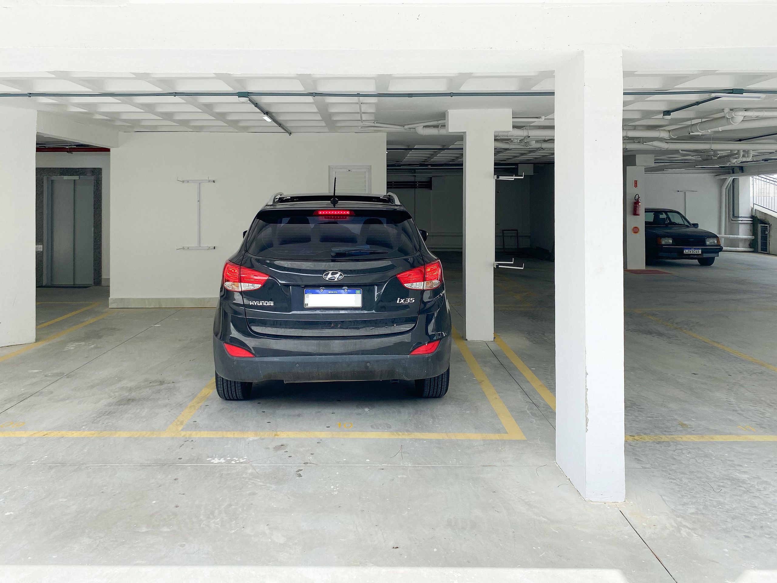 A black car parked in a parking garage with white pillars and a concrete floor.