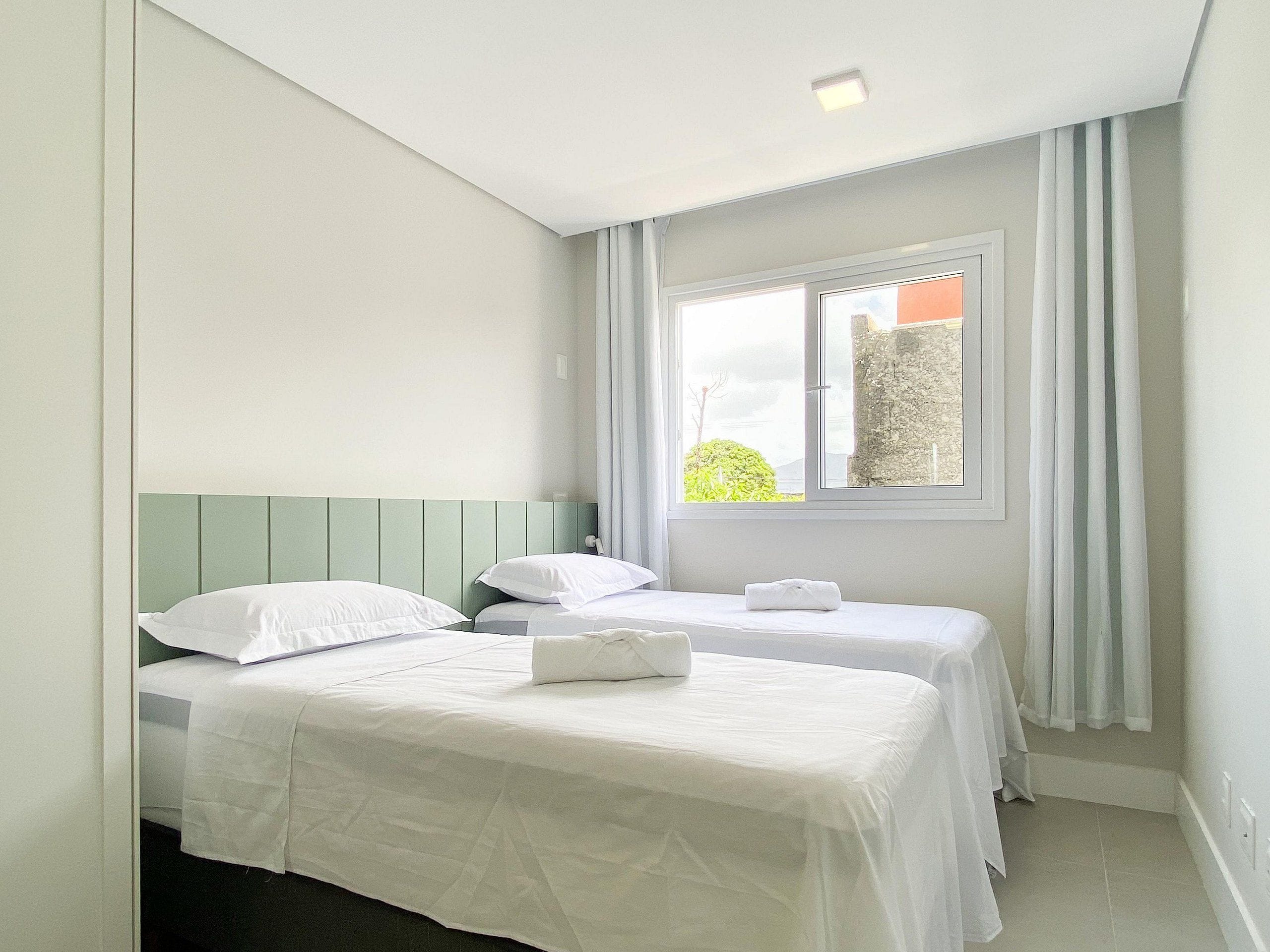 Un dormitorio con dos camas individuales, una ventana con cortinas y vistas al exterior.