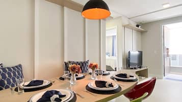 Un comedor con una mesa larga dispuesta para cuatro personas, un televisor sobre un mueble bajo y una lámpara colgante moderna.
