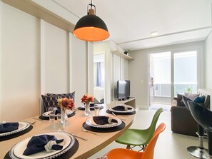 A dining area with a round table set for four, a television, and a balcony with a view. - Apê Cheio de Estilo - Campeche (Florianopolis)