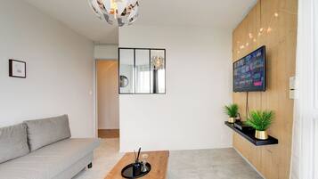 Een moderne woonkamer met een grijze bank, een houten salontafel, een aan de muur bevestigde televisie en een decoratieve spiegel.