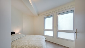 Une chambre à coucher avec un lit, deux fenêtres et une porte.