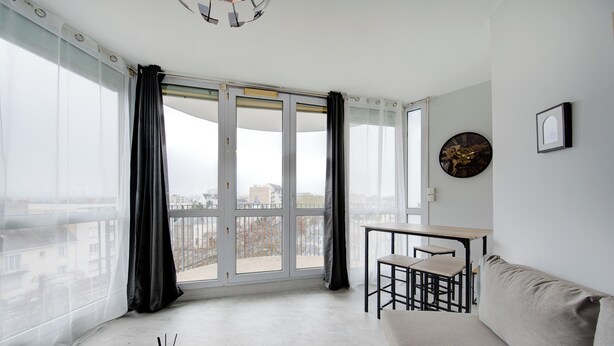 Un salon moderne avec un canapé, une petite table et un balcon agrémenté de rideaux.