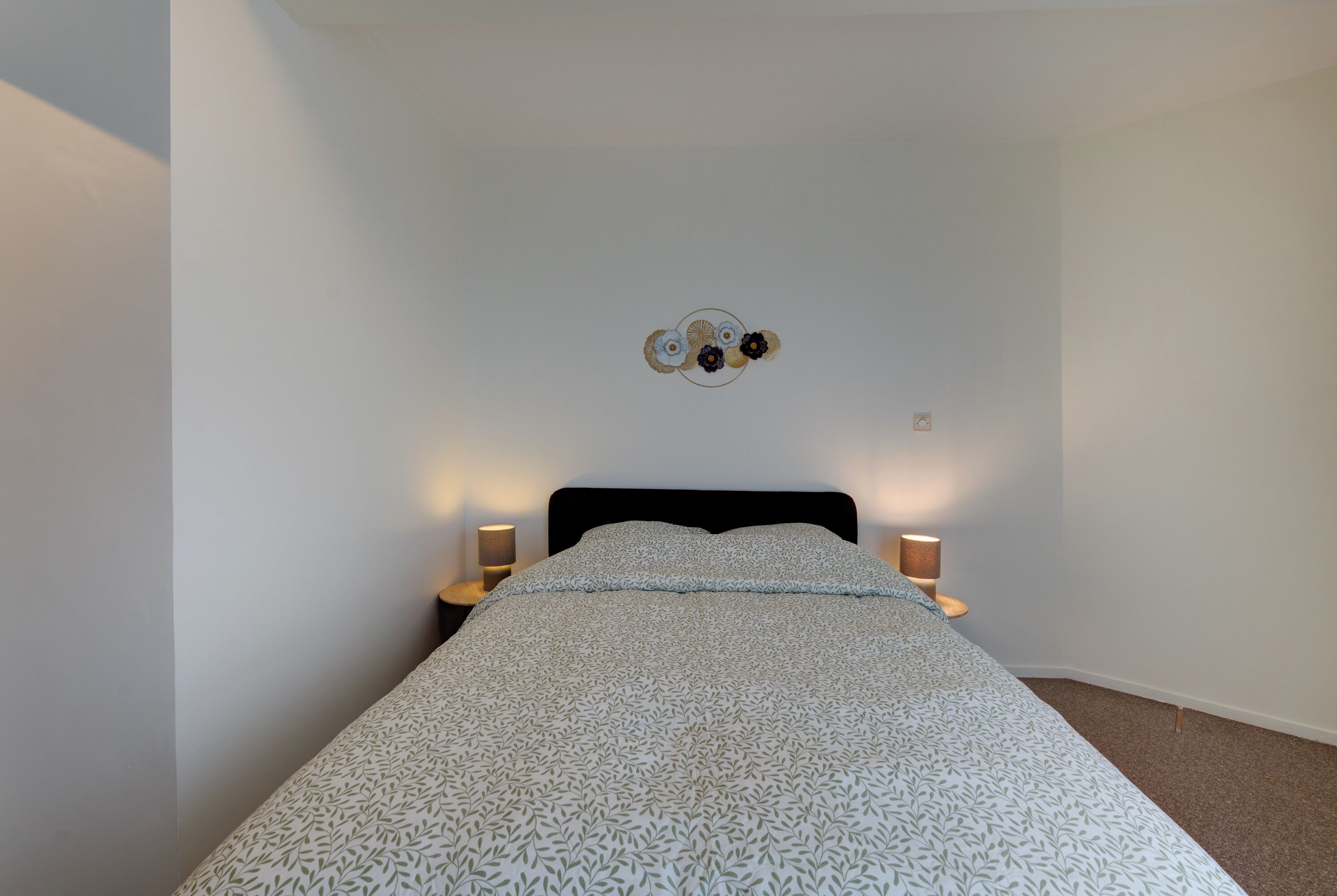 A neatly made bed with a patterned bedspread, two bedside lamps, and a wall-mounted decoration above the bed.