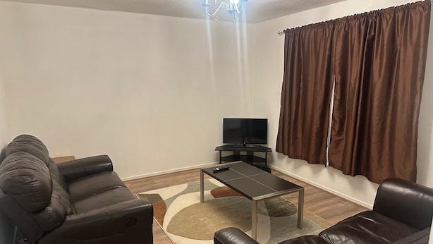 A living room with a sofa, a coffee table, a TV, and a window with curtains. - Honeyhill Retreat in Peterborough (Peterborough)