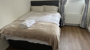 A neatly made bed with a beige duvet, a rolled white towel, and a dark headboard. - Honeyhill Retreat in Peterborough (Peterborough)
