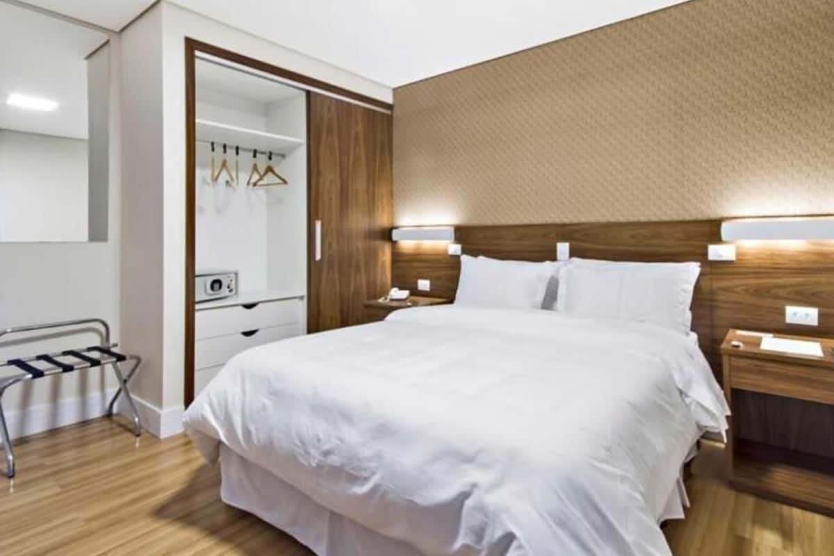 Une chambre d’hôtel avec un grand lit, une tête de lit en bois, des tables de chevet, un miroir et une armoire.