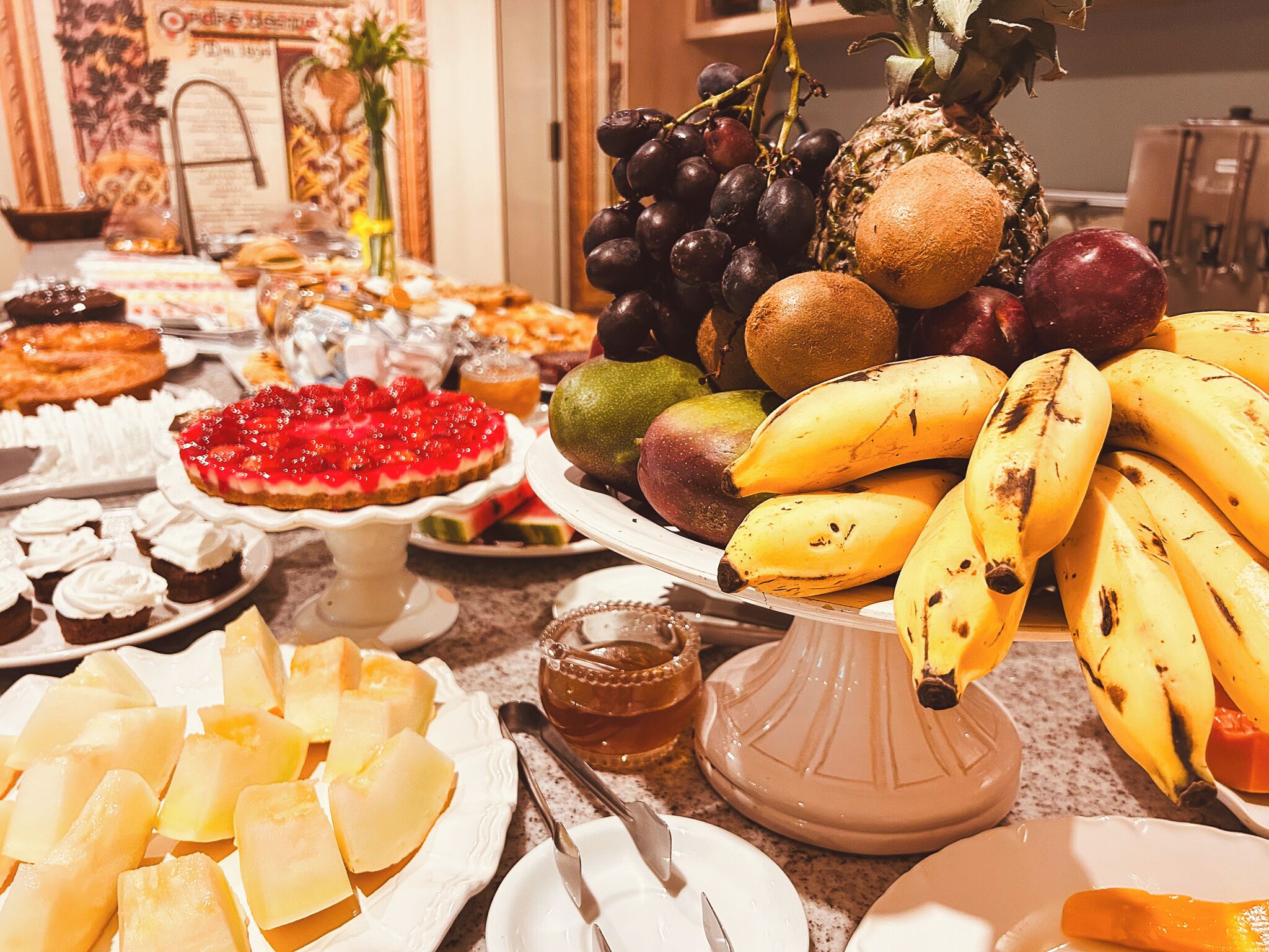 A buffet with various dishes including fruits, desserts, and a cake.