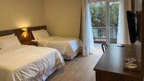 A hotel room with two beds, a desk, and a large window with curtains.