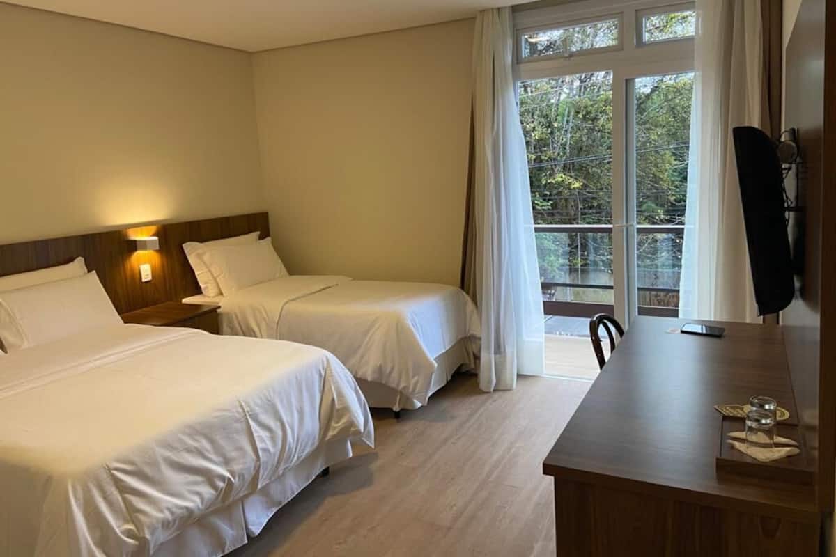 Une chambre d’hôtel avec deux lits, un bureau et une grande fenêtre avec des rideaux.