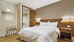 A neatly arranged hotel room with a large bed, wooden headboard, bedside tables, a mirror, and a wardrobe.
