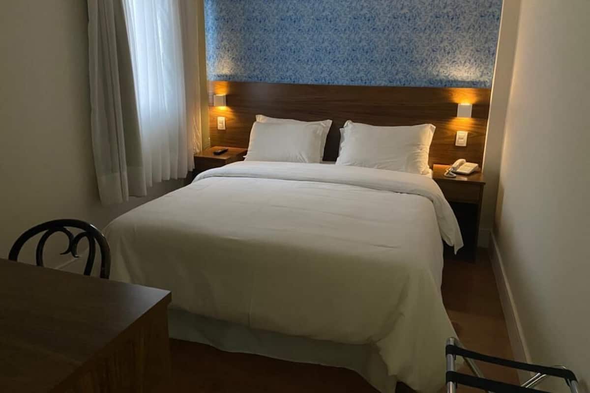 Une chambre d’hôtel avec un grand lit, deux tables de chevet avec des lampes, une tête de lit en bois et un mur orné d’un motif.