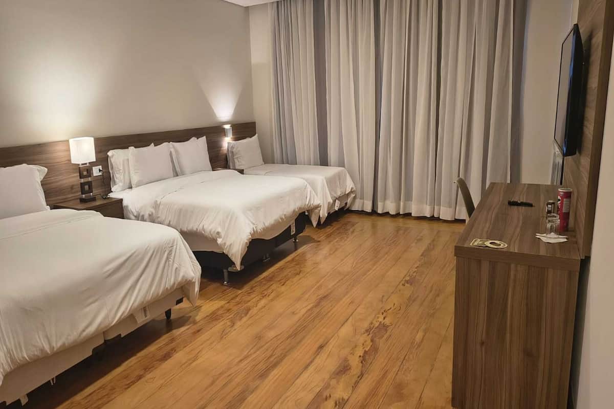 Une chambre d’hôtel avec trois lits, un plancher en bois, un bureau et une télévision.