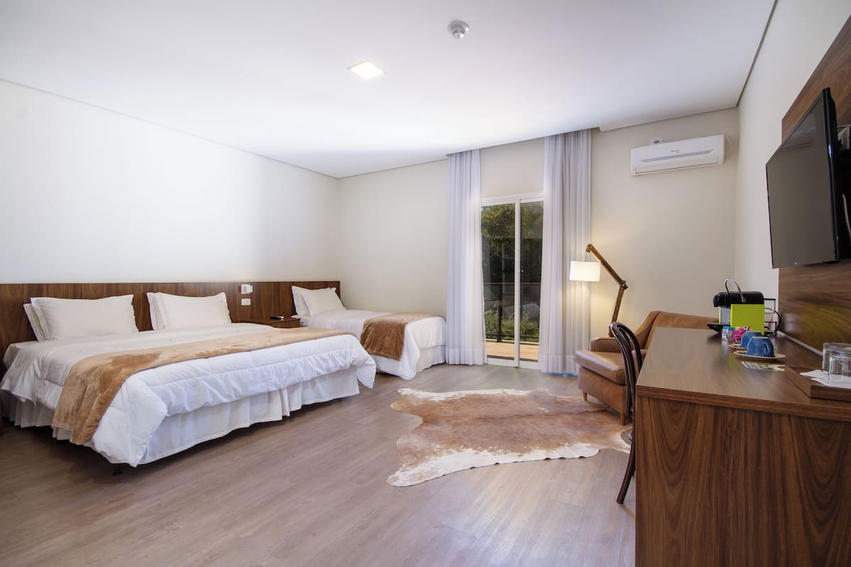 Une chambre d’hôtel avec deux lits, un bureau en bois, une télévision et une porte-fenêtre coulissante donnant sur l’extérieur.